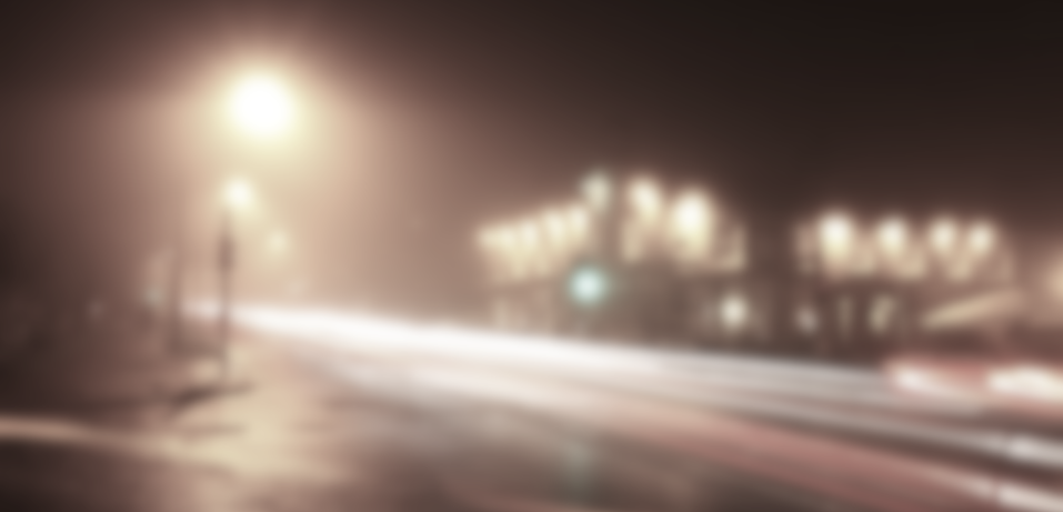 Street in London at night, significantly blurred. Showing street lights, a road and building in the background.